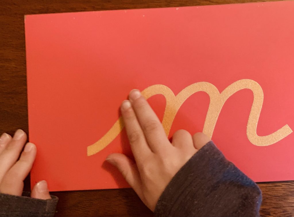Child tracing cursive sandpaper letter "m".